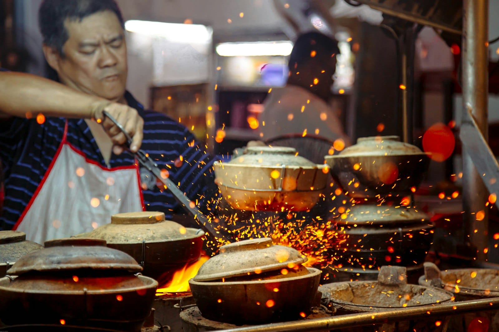A cook tending clay pots at a night food stall