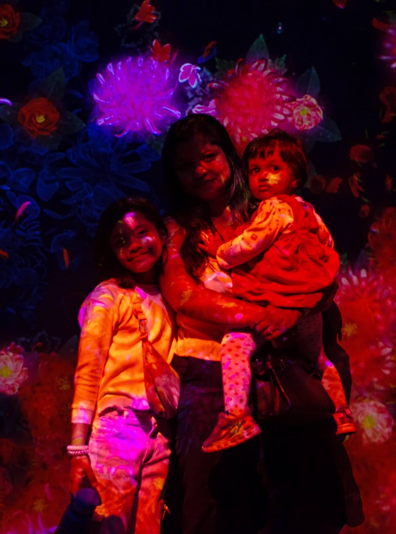 A mother with her two daughters inside a glowing flower-projection art room
