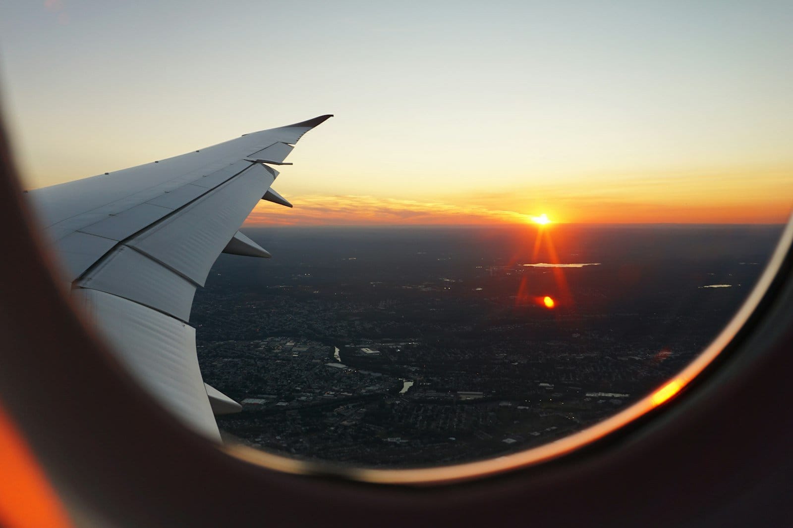 Sun setting beyond an aeroplane wing seen through a cabin window