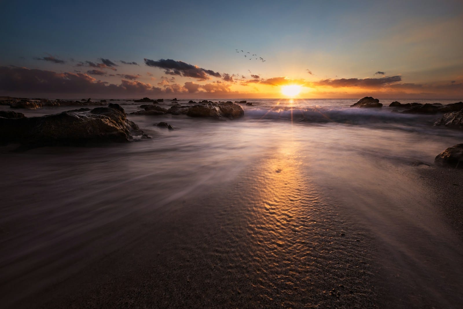 Golden sunset over rocks and gentle surf at Boucan Canot beach on Réunion's west coast