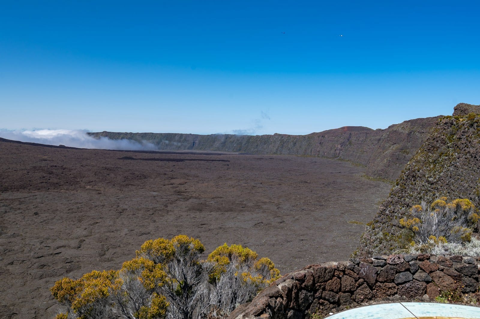 Wide dark lava plain and caldera rim around Piton de la Fournaise volcano under a clear blue sky