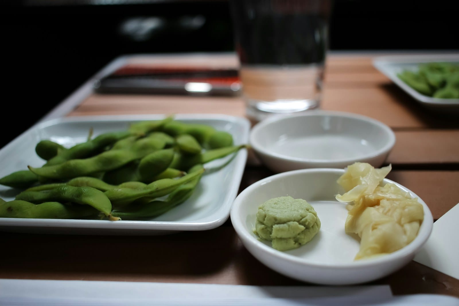 Edamame served alongside wasabi and pickled ginger on a restaurant table.