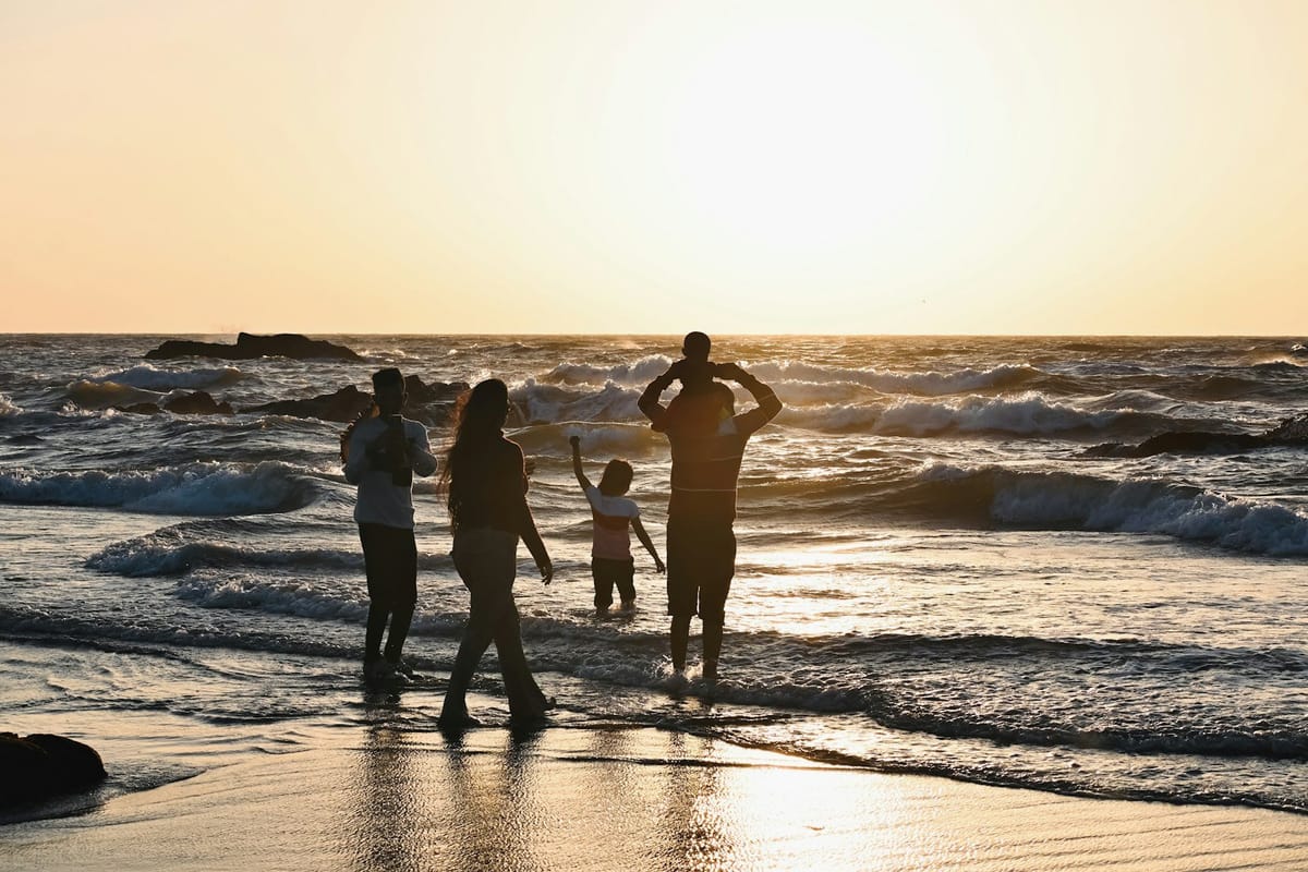 A family silhouetted against golden waves on a beach at sunset.