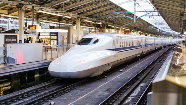 A white Shinkansen bullet train at a bright station platform in Japan.