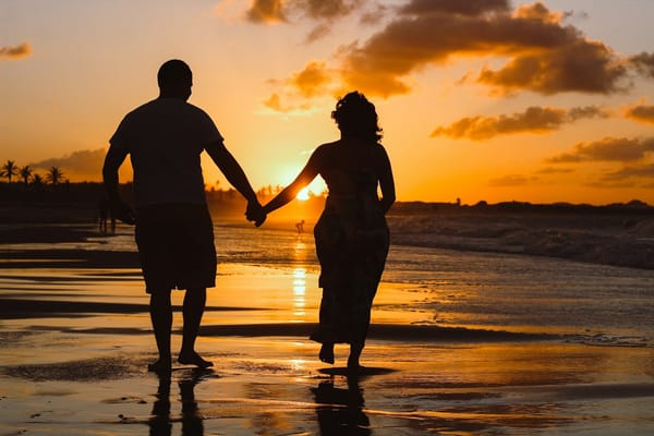 A couple walking hand in hand on a beach at golden hour.