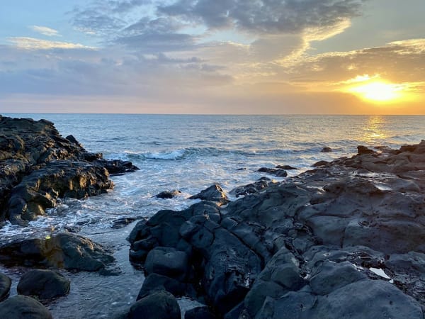 Golden sunset over waves and dark rocks on the Jeju coastline