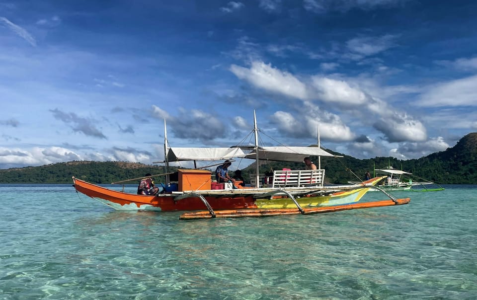 A traditional orange bangka boat floating on clear turquoise water off a Philippine island